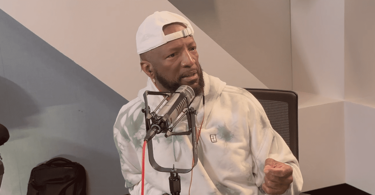 Man speaking into a microphone, wearing cap.